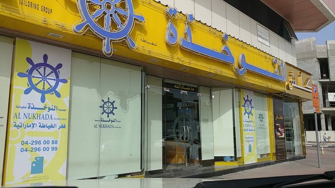 The shop sign: Al Nukhada Tailoring Group, with the ship's wheel and phone number