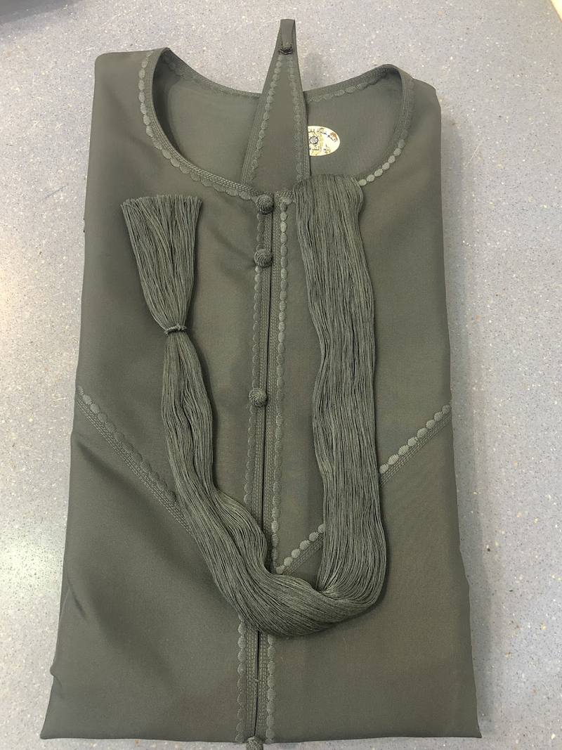 An olive kandura with a long tarboosha tassel on a mannequin in the shop