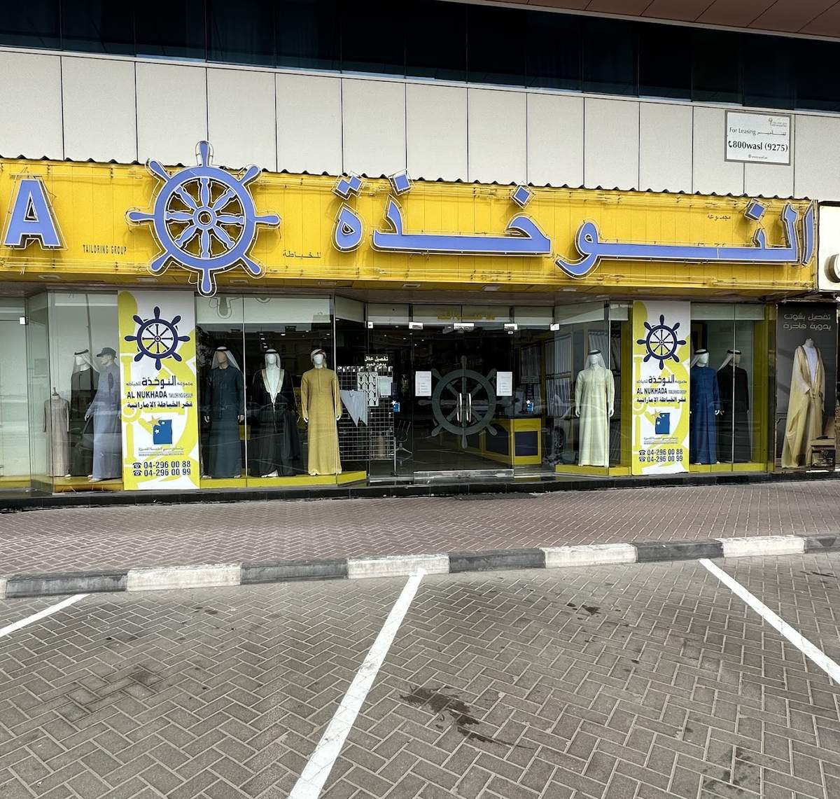 The Al Nukhada shopfront on Al Wuheida Street: yellow fascia, blue ship's wheel and kanduras in the windows