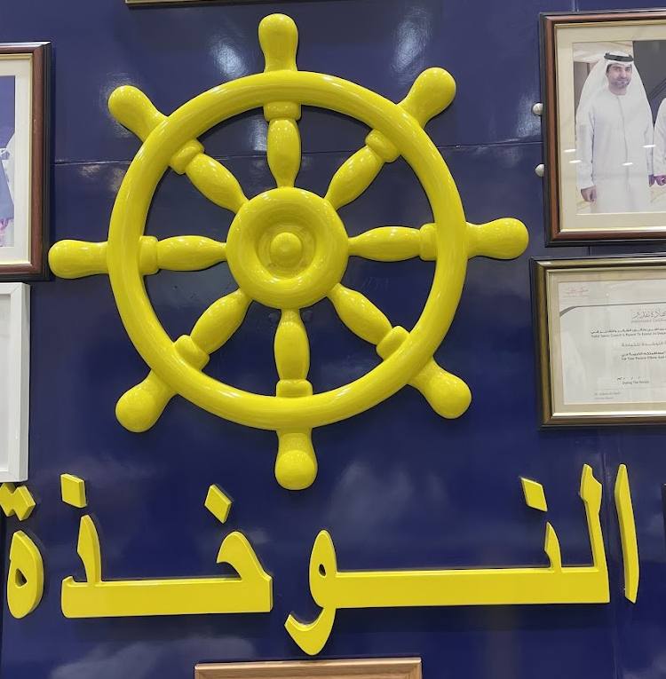 The ship's wheel and the name النوخذة on the wall inside the shop